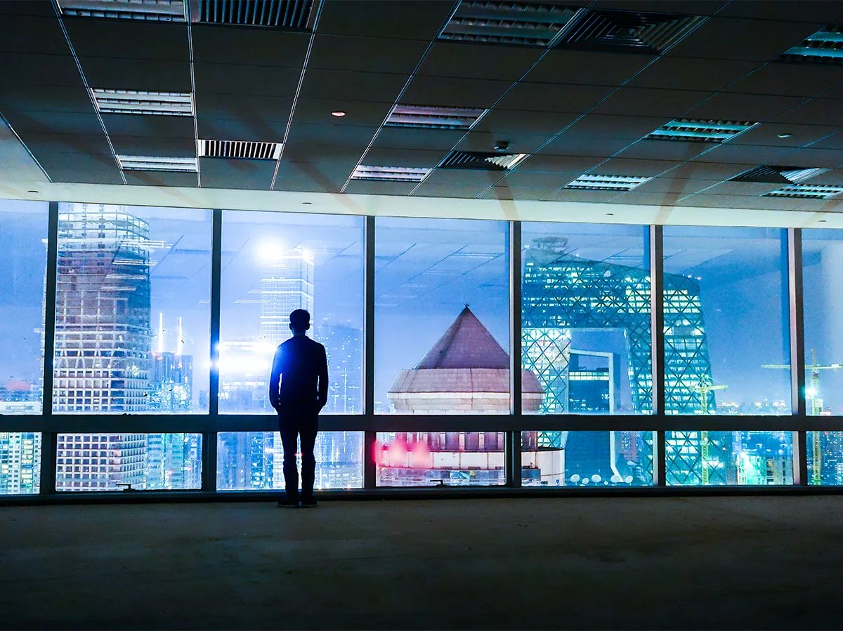 silhouette of person looking out office building window onto nighttime city scape